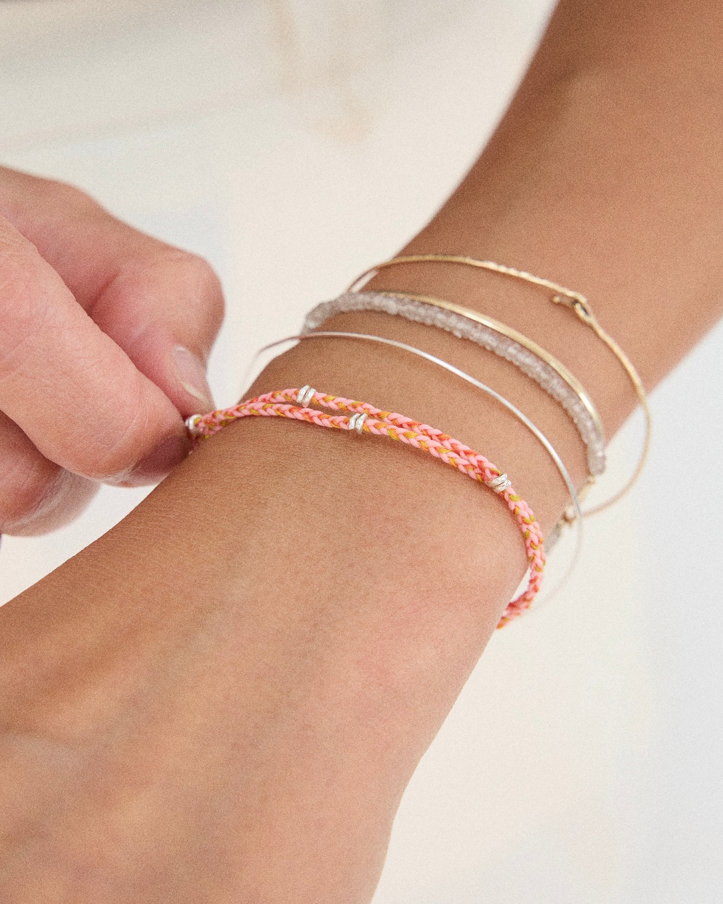 Pink braided bracelet styled with layered silver bracelets on wrist