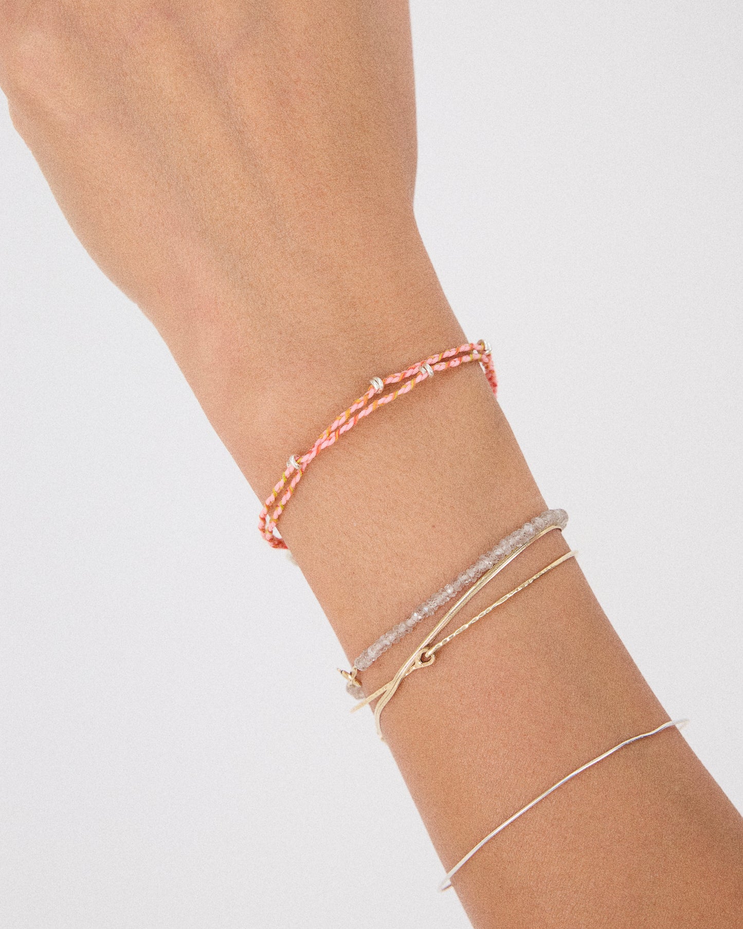 Woman wearing pink woven bracelet layered with fine silver jewelry