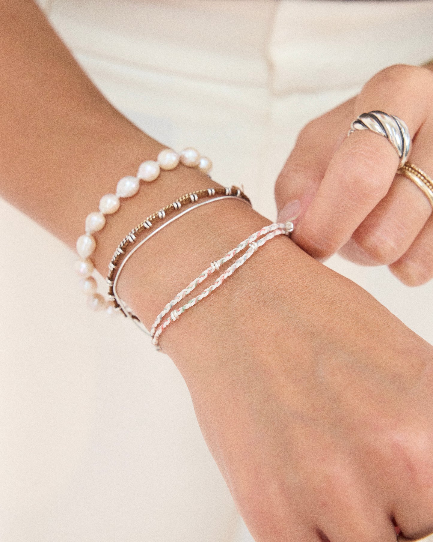 Pastel friendship bracelet layered with pearl bracelet and silver jewelry for everyday styling