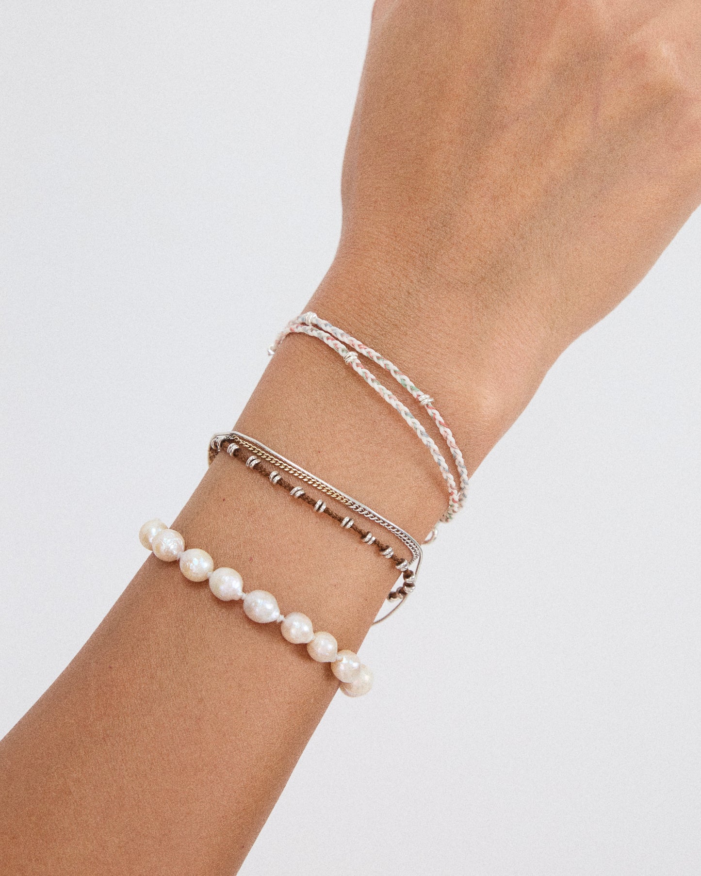 Pastel braided bracelet layered with pearl and silver bracelets for a feminine everyday jewelry look