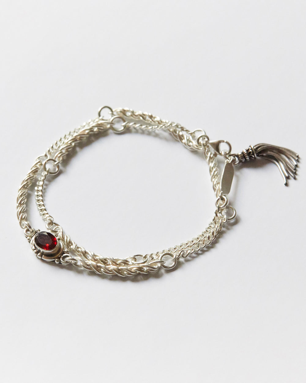 silver bracelet with twisted chain texture and red gemstone detail on white background