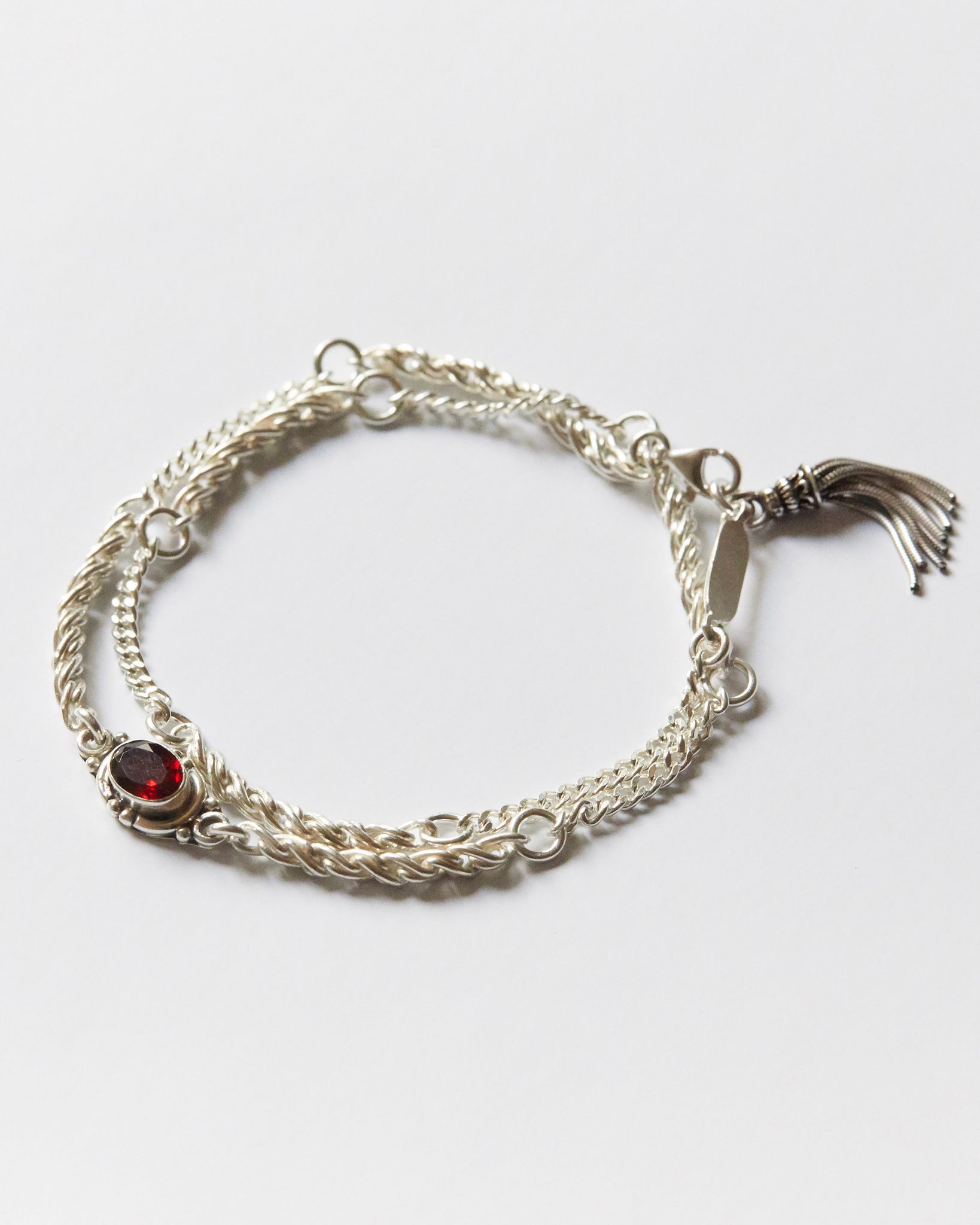 silver bracelet with twisted chain texture and red gemstone detail on white background