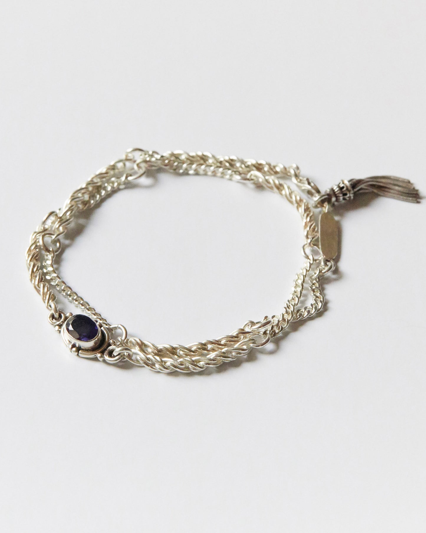 silver bracelet with twisted chain texture and purple gemstone detail on white background
