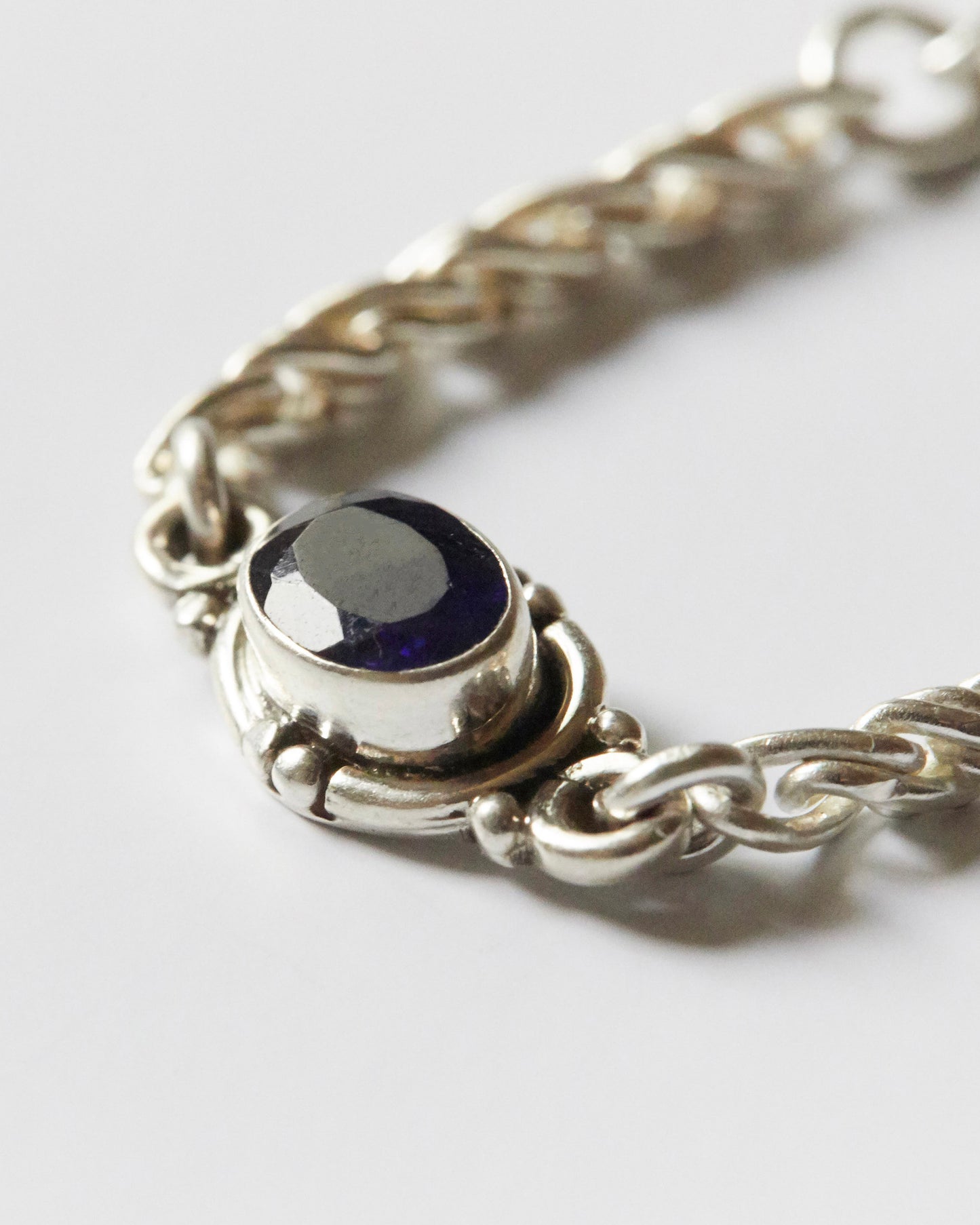 close-up of purple gemstone set in silver chain bracelet showing texture and detail