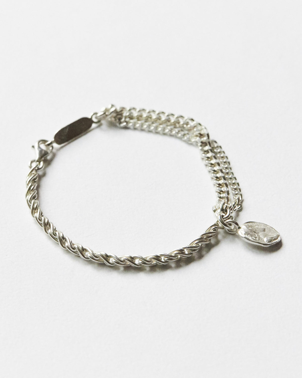 Silver chain bracelet with two distinct chain textures and an irregular coin charm, showcasing its layered structure and sculptural details.