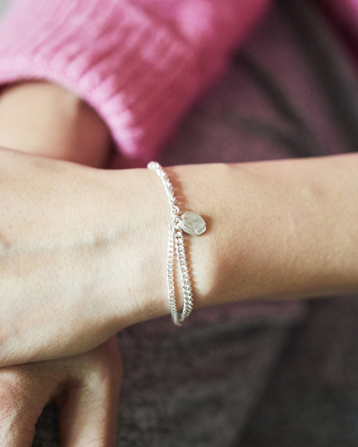 Minimalist silver chain bracelet with a coin pendant charm, styled on the wrist for an understated everyday jewelry look.