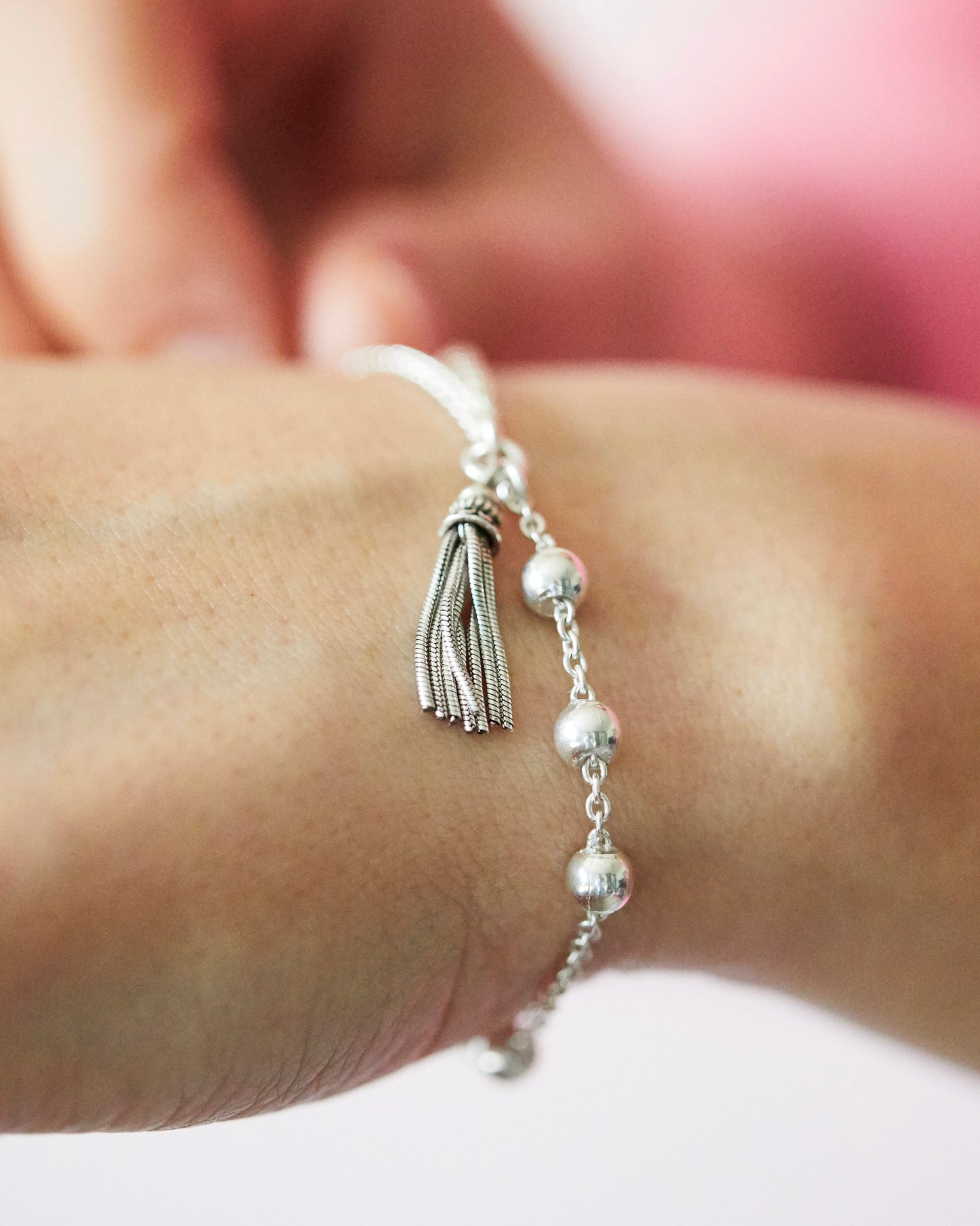 silver bracelet with tassel charm on a wrist against a blurred background