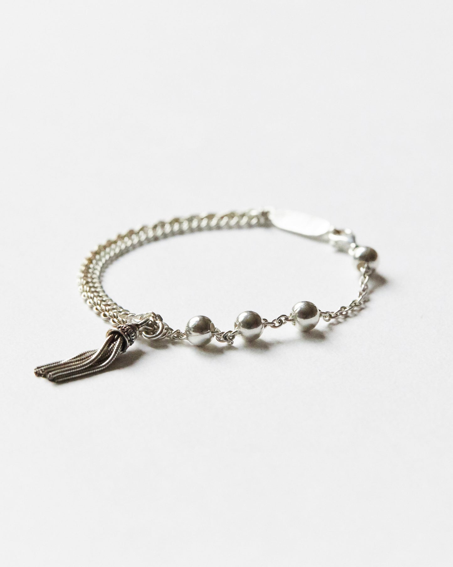 silver bracelet with bead accents and tassel detail on white background