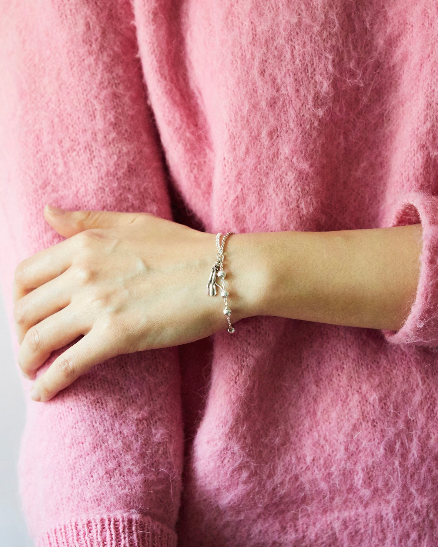silver chain bracelet with small beads and tassel styled on wrist with soft pink sweater