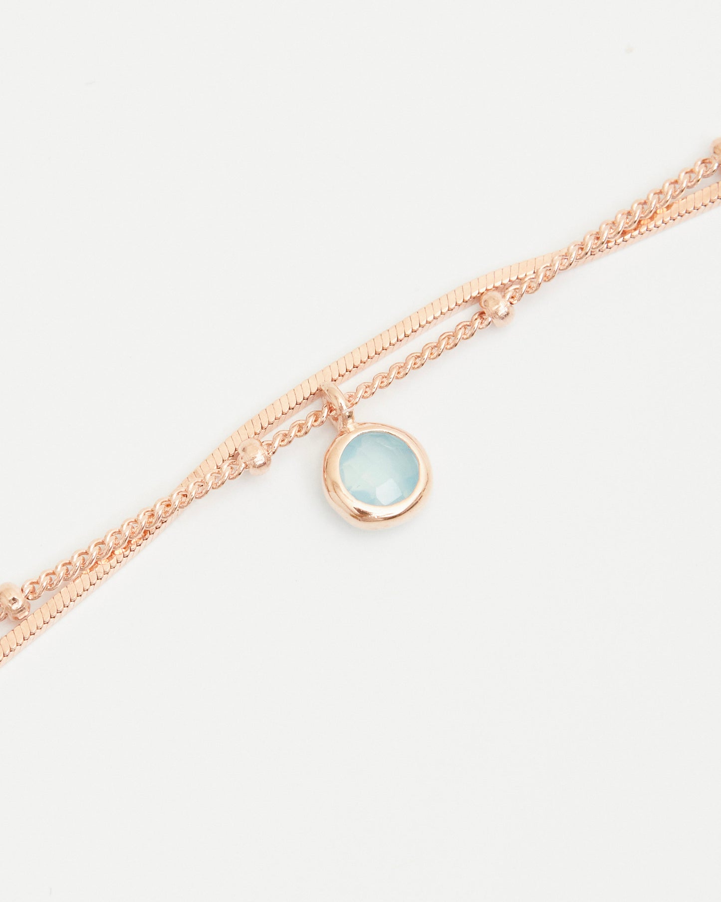 Close-up of blue gemstone charm on layered rose gold bracelet