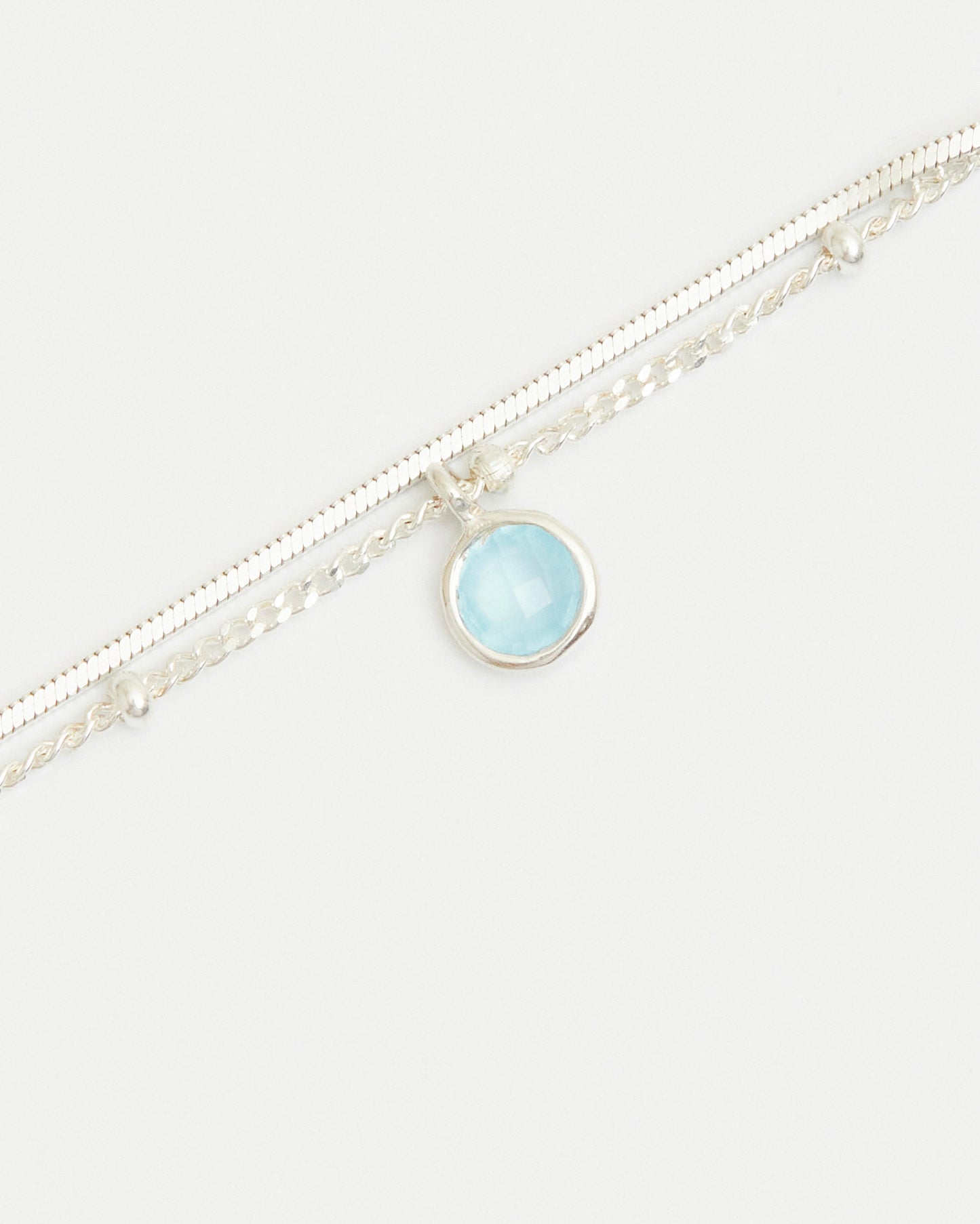 Close-up of blue gemstone charm on layered sterling silver bracelet