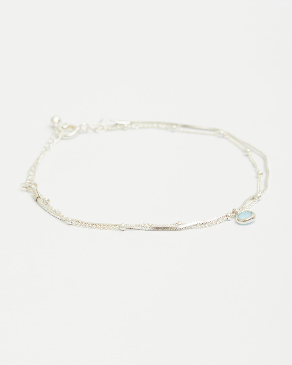Sterling silver layered bracelet with blue gemstone charm on white background