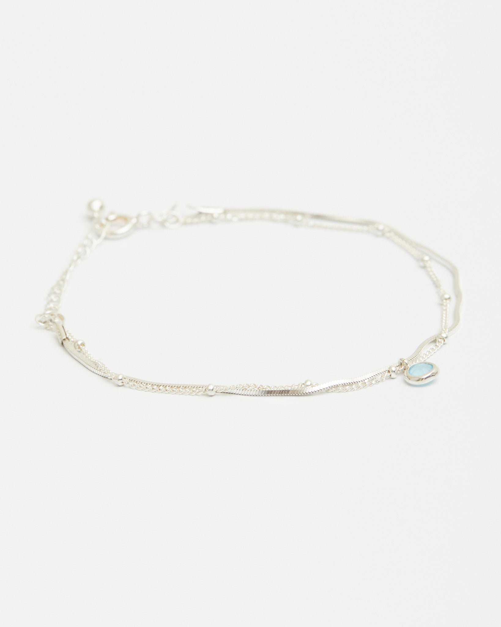 Sterling silver layered bracelet with blue gemstone charm on white background