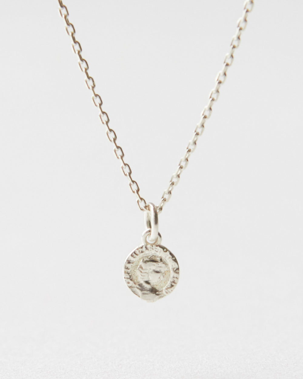 Close-up of a silver coin pendant necklace resting on white surface