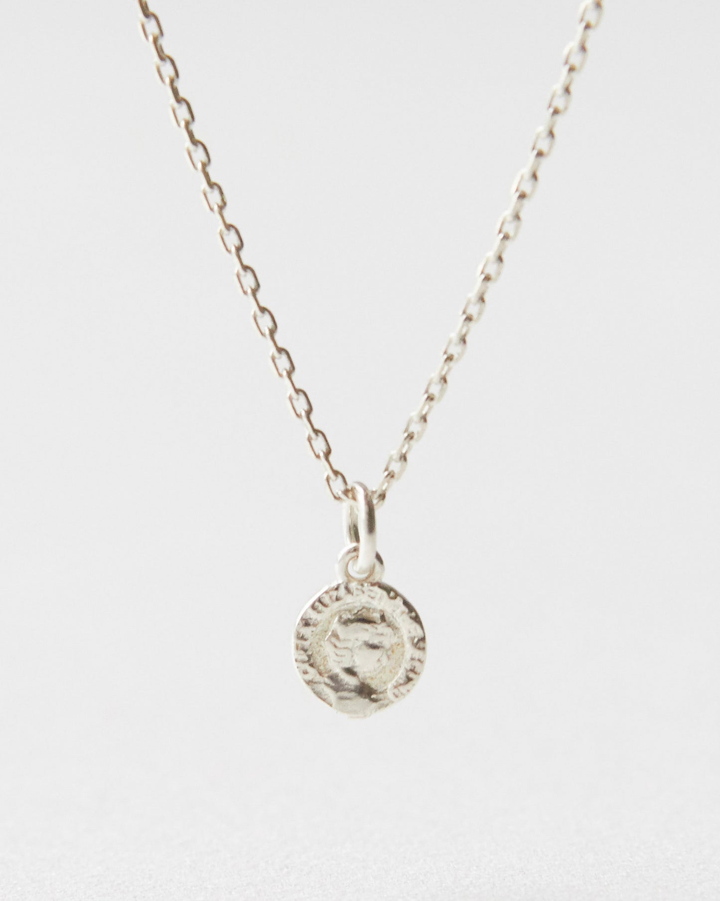 Close-up of a silver coin pendant necklace resting on white surface