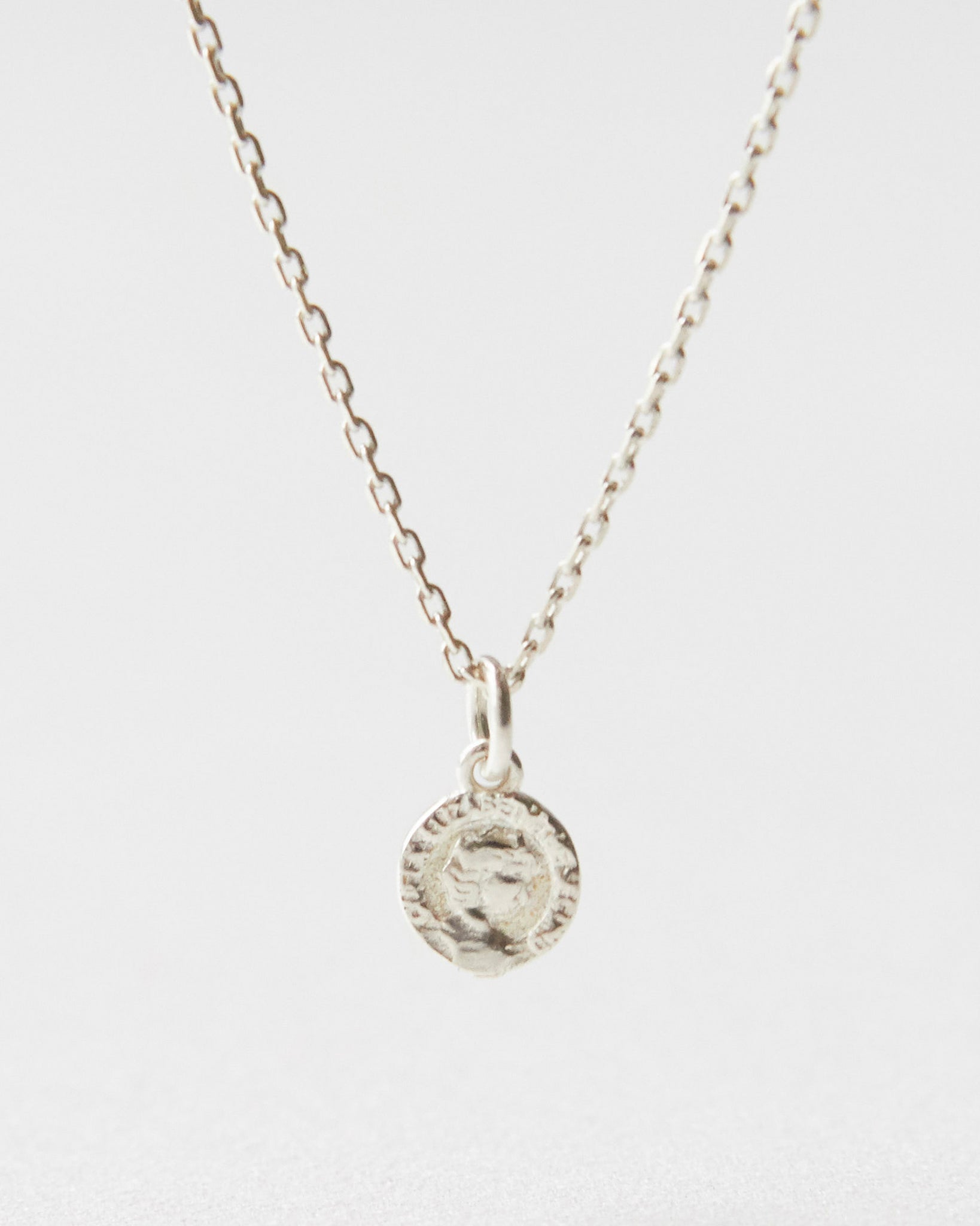Close-up of a silver coin pendant necklace resting on white surface