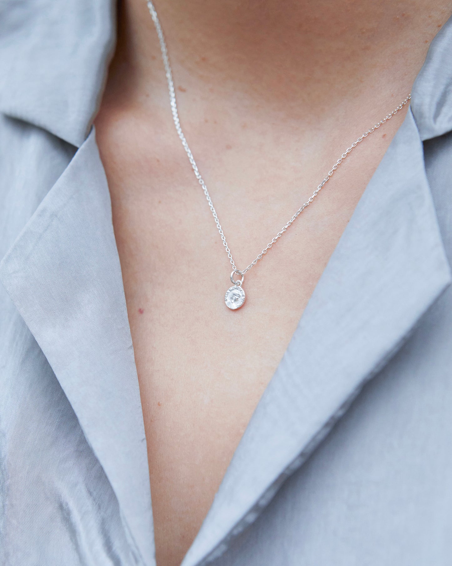 Model wearing a delicate silver coin necklace against a light grey blouse