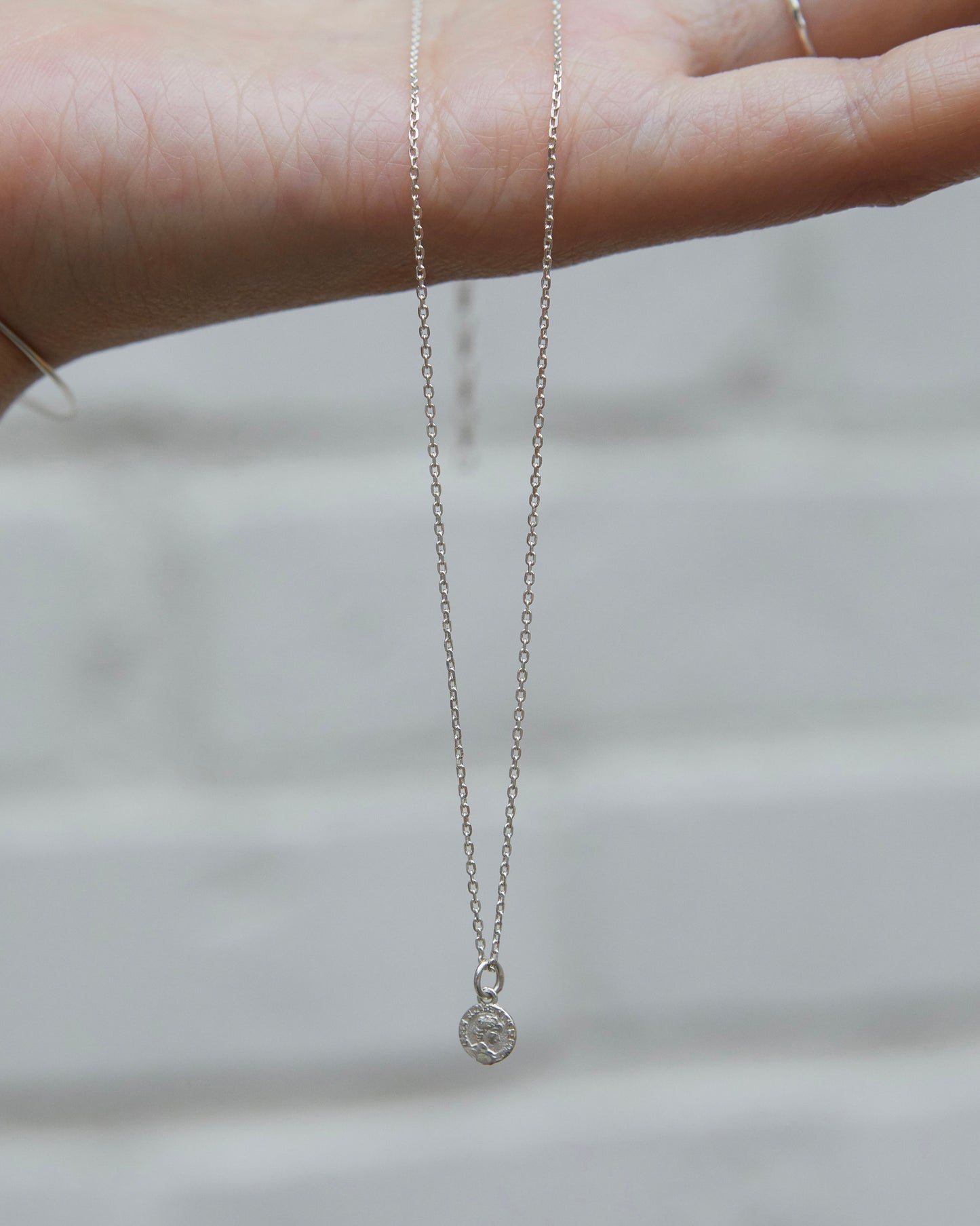 Sterling silver coin pendant necklace suspended from a hand