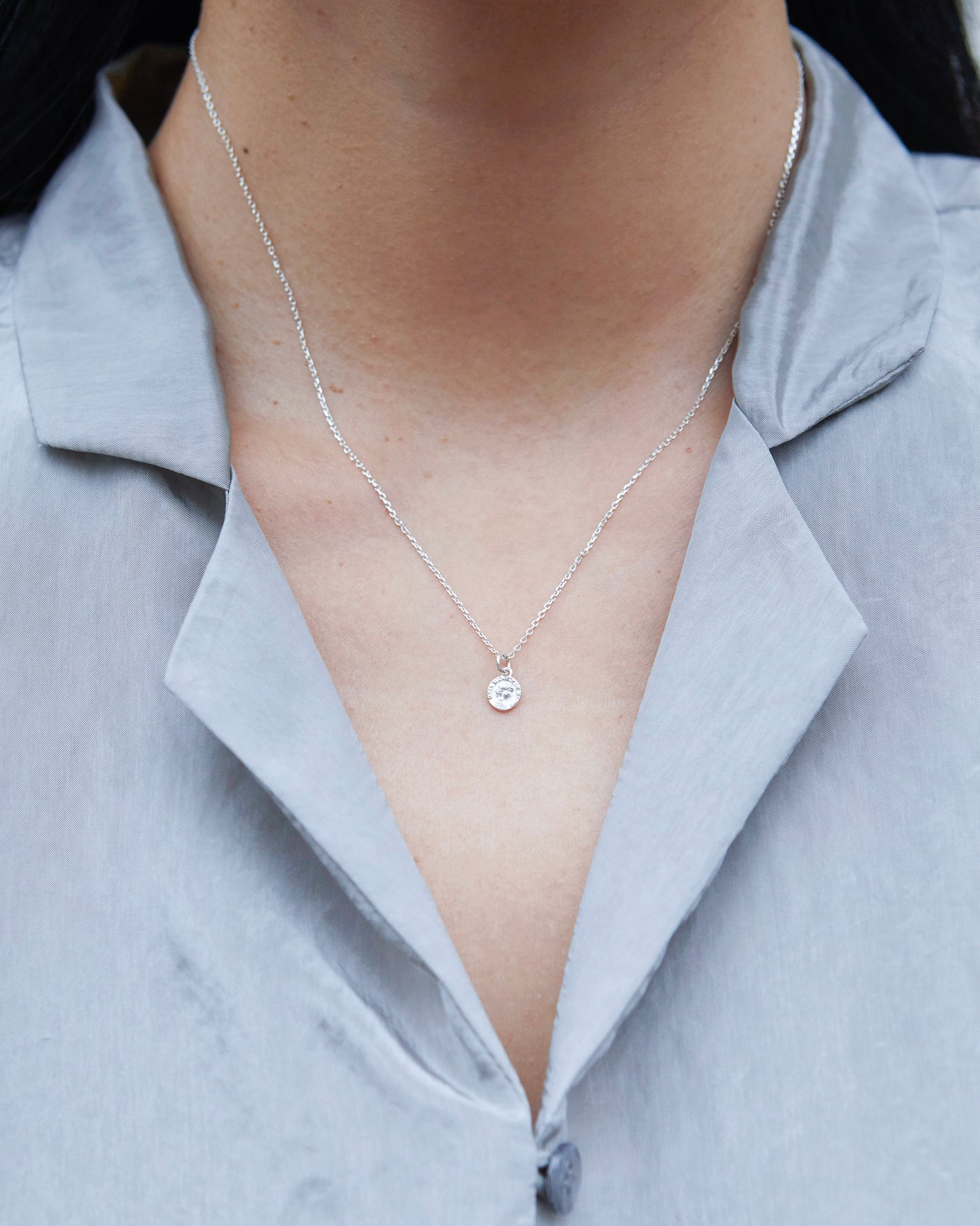A round coin-like silver pendant featuring engraved details and fine chain