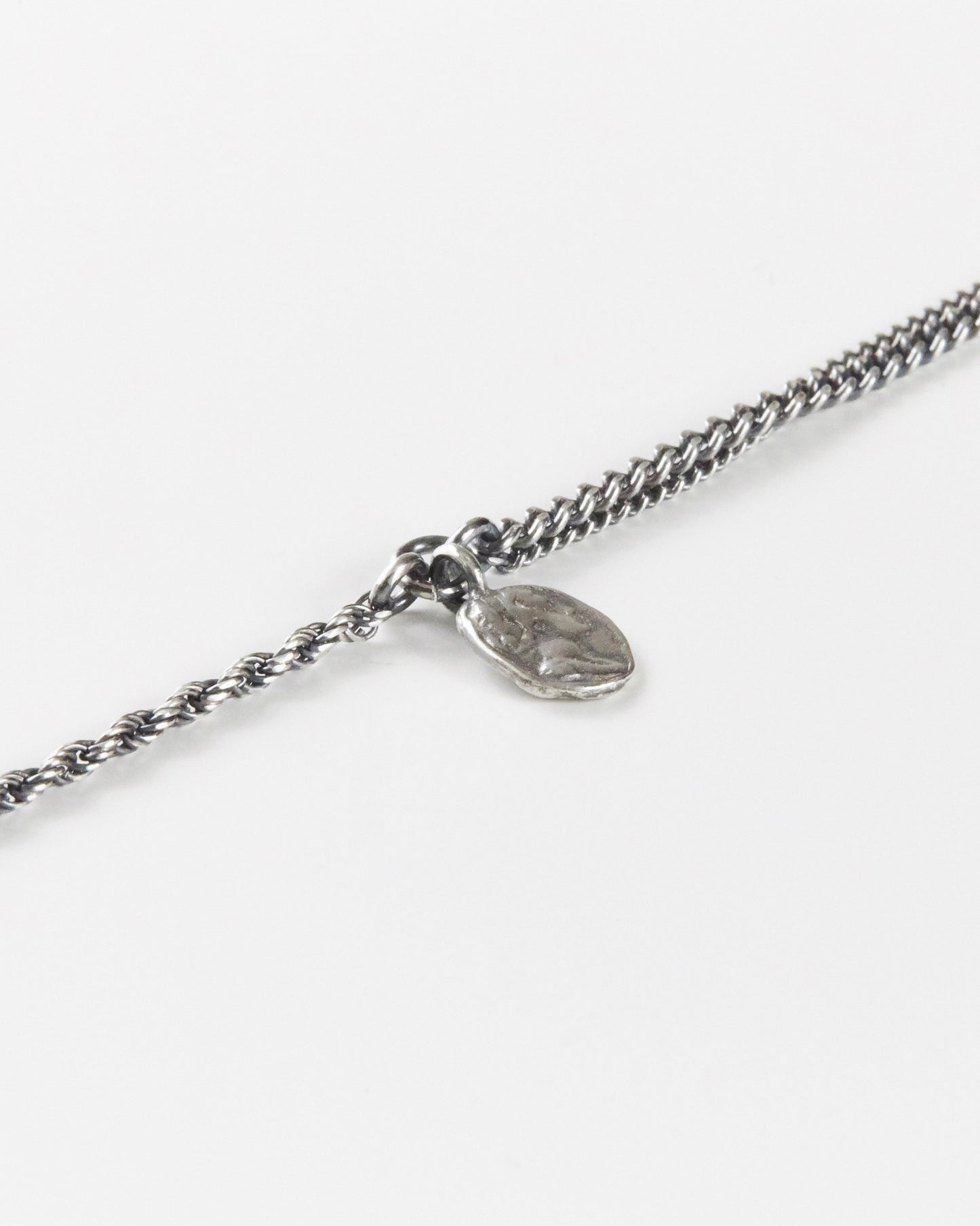 Close-up of handmade textured coin pendant on 925 silver bracelet, dual chain detail