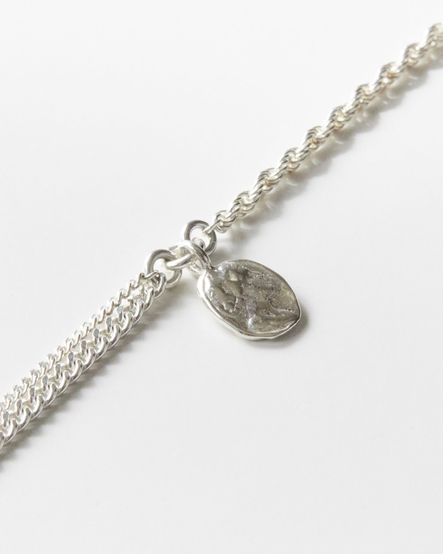 Close-up of handmade textured coin pendant on 925 silver bracelet, dual chain detail