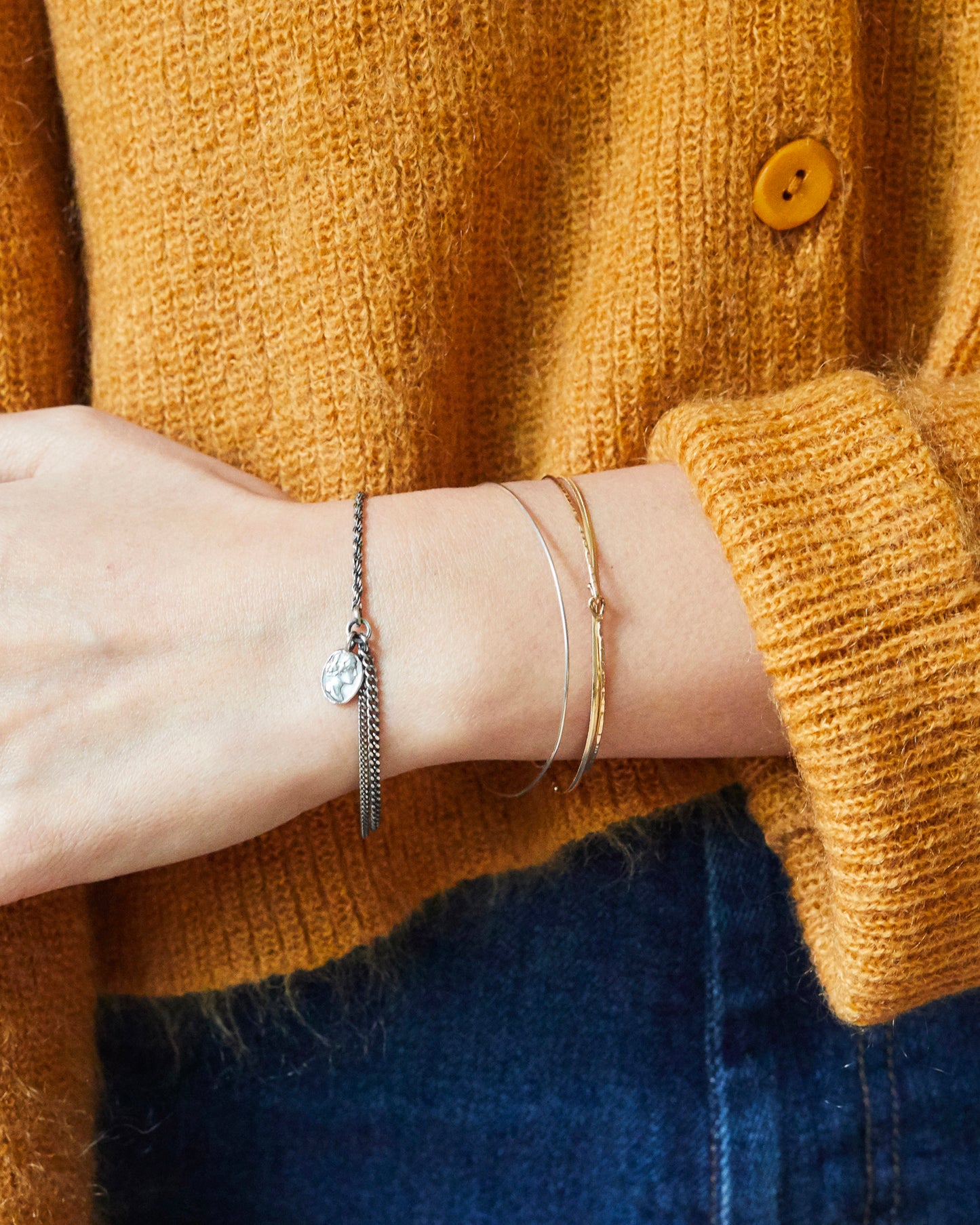 Hand wearing B507 silver bracelet with hammered coin charm, styled with cozy knitwear
