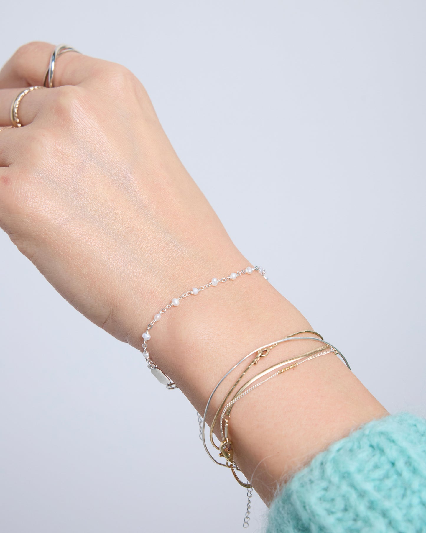 Minimal sterling silver pearl bracelet worn on wrist with layered jewelry