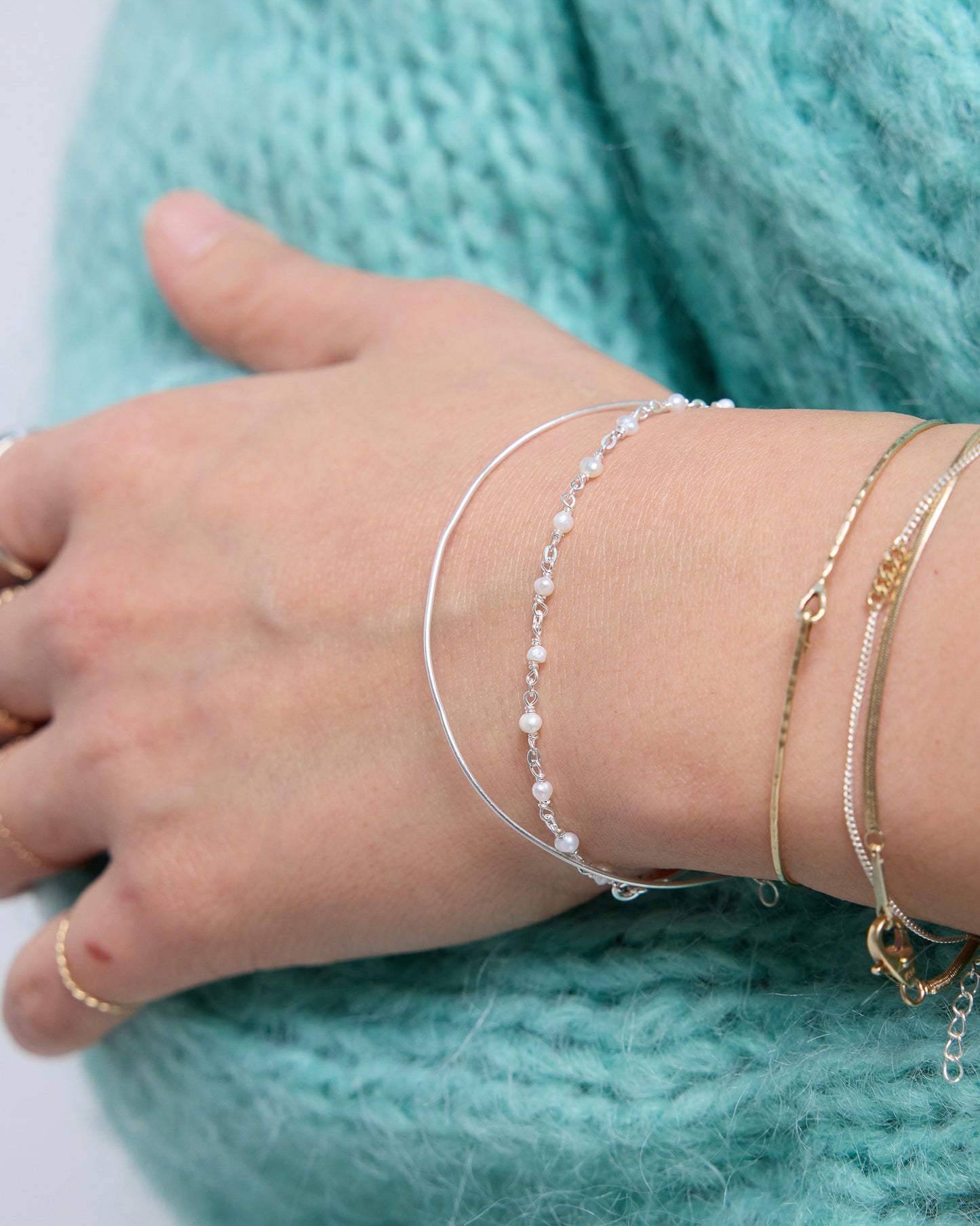 Delicate sterling silver pearl bracelet layered on wrist with cozy knit styling