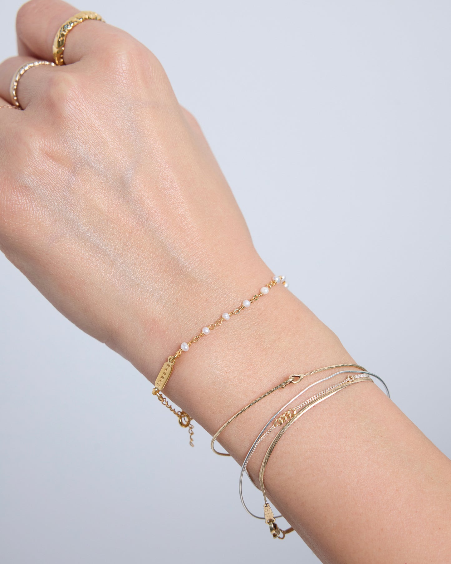 Minimal gold pearl bracelet worn with layered chain bracelets
