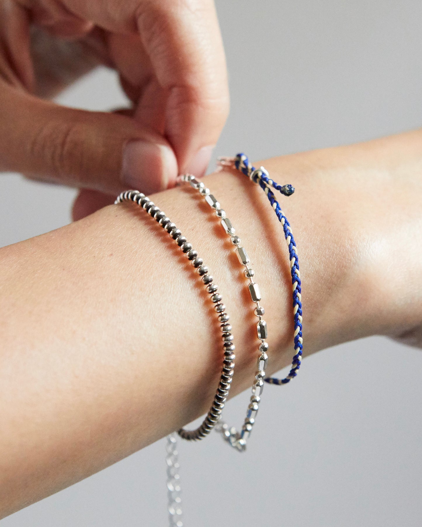 Close-up of a wrist wearing multiple bracelets on a neutral background