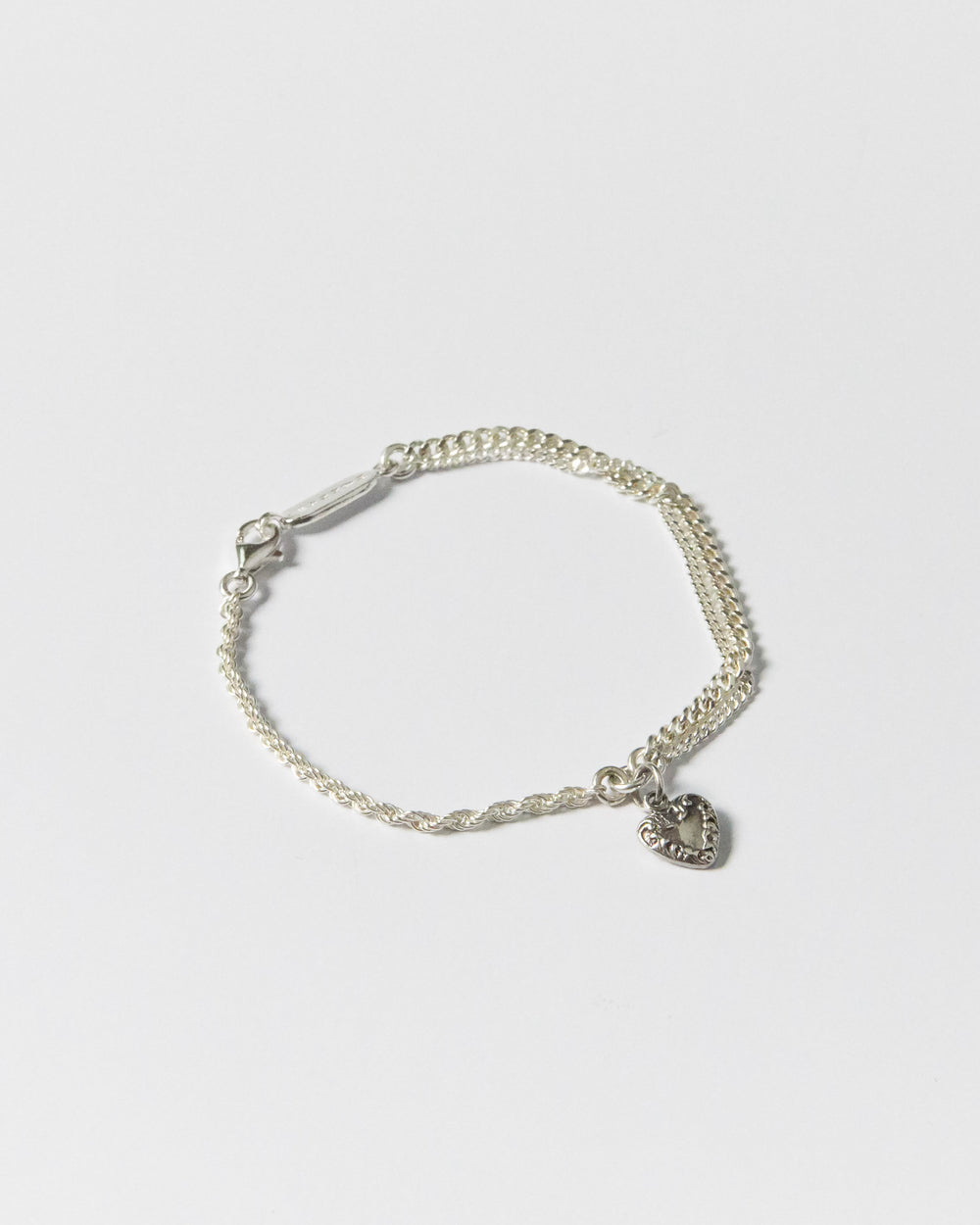 Flat lay of handcrafted silver bracelet with twisted and curb chains, featuring heart charm