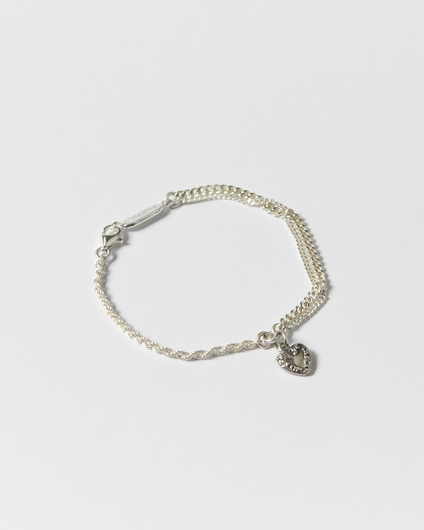 Flat lay of handcrafted silver bracelet with twisted and curb chains, featuring heart charm