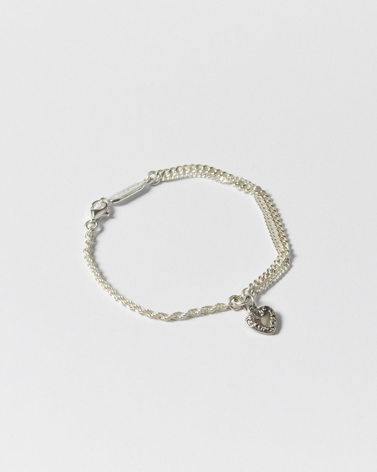 Flat lay of handcrafted silver bracelet with twisted and curb chains, featuring heart charm