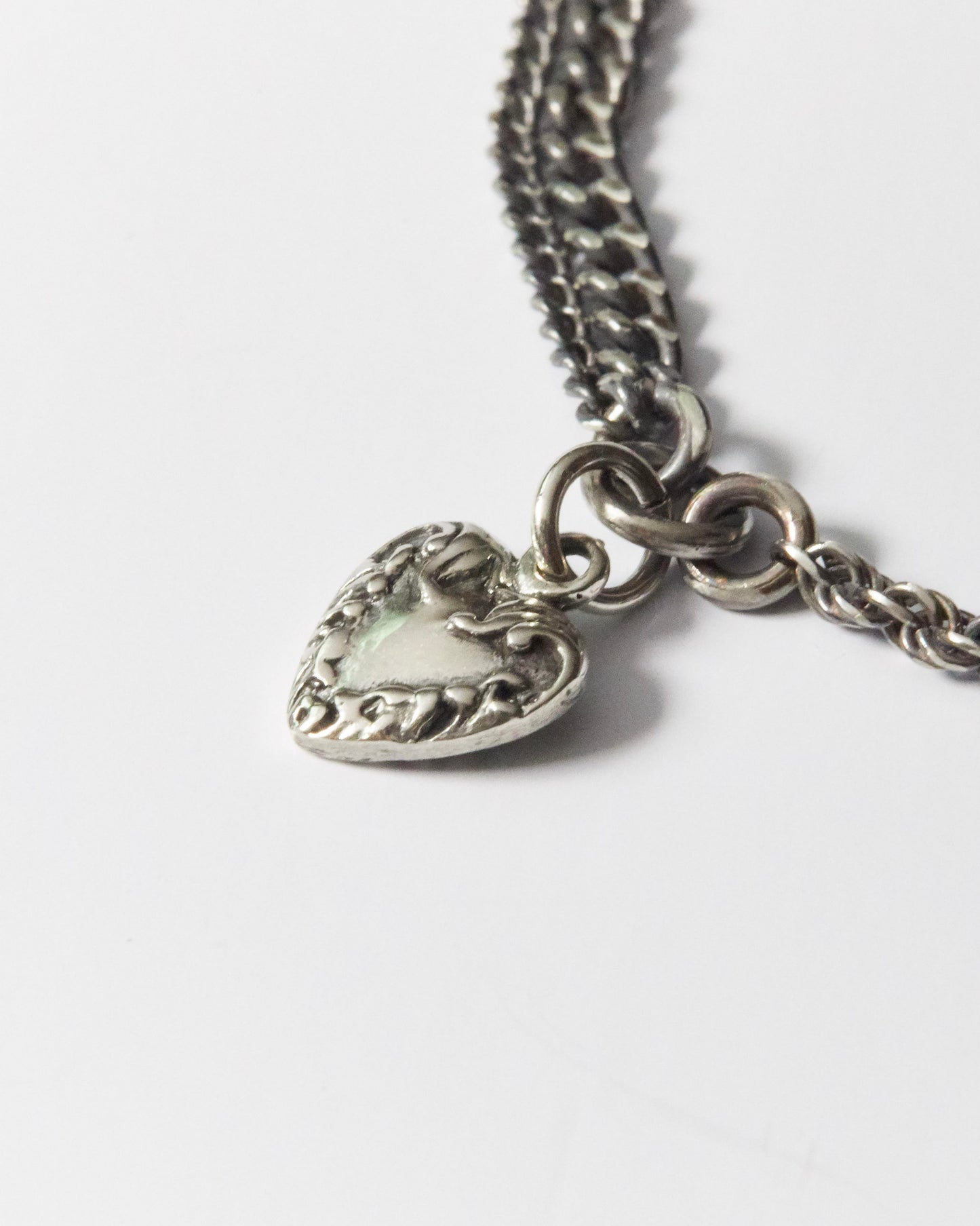 close-up of detailed silver heart pendant with floral etching on dual-chain bracelet