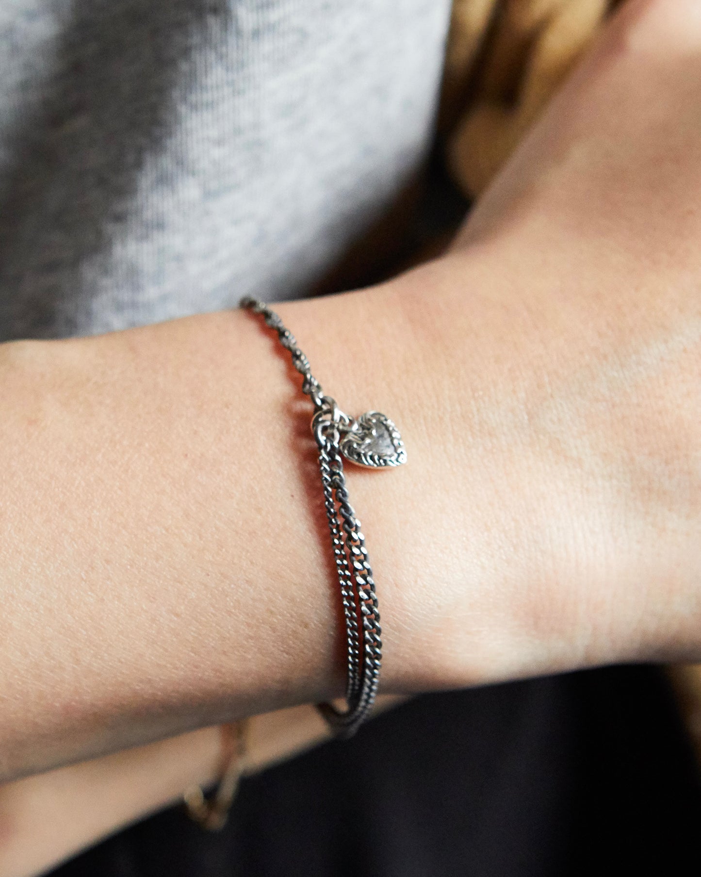 Minimalist silver bracelet with heart charm worn on wrist, paired with neutral outfit