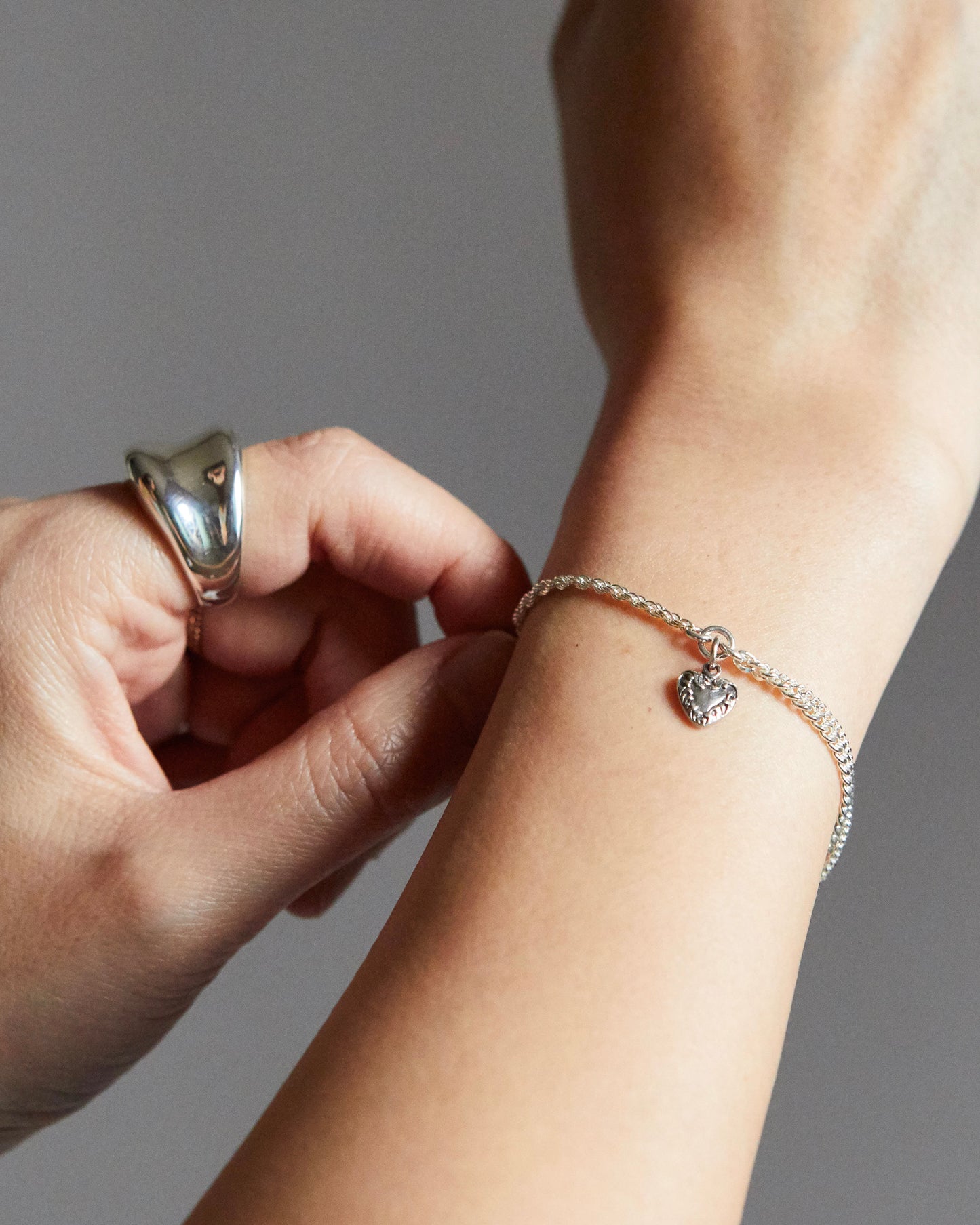 Person adjusting a silver bracelet on their wrist with a neutral background