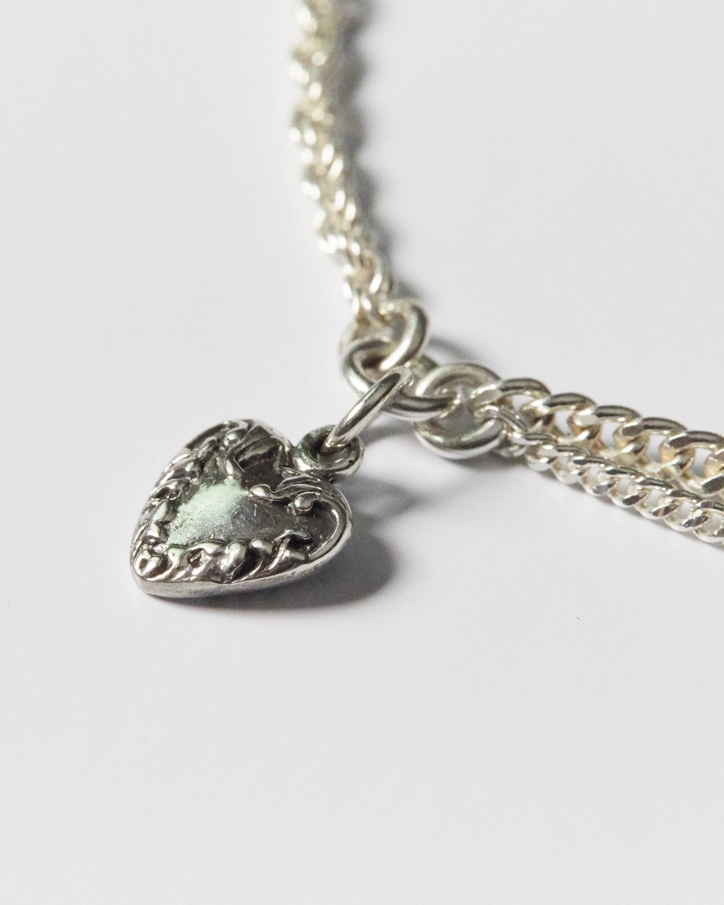 close-up of detailed silver heart pendant with floral etching on dual-chain bracelet