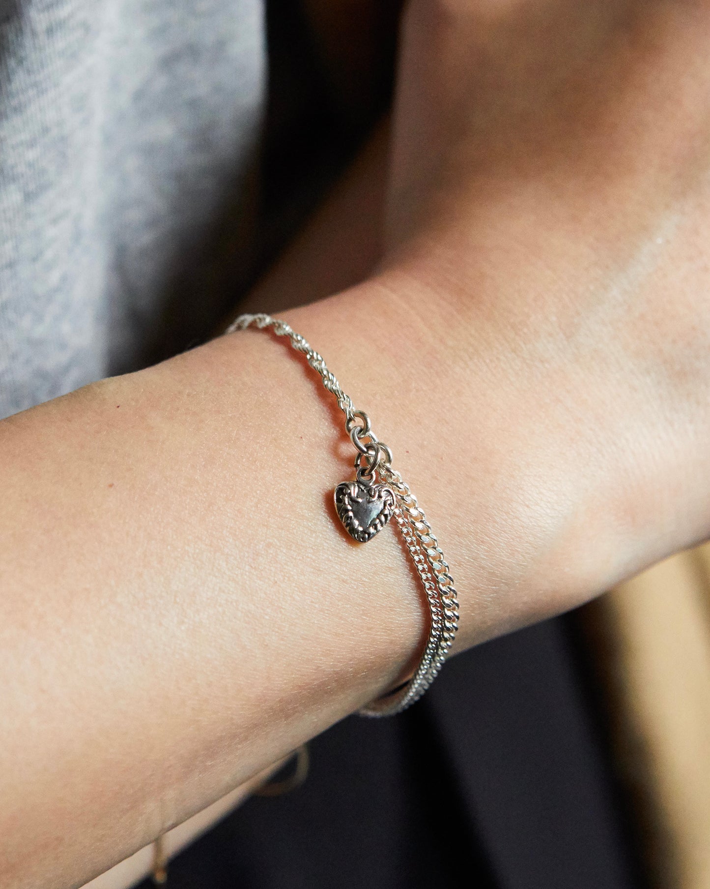 Minimalist silver bracelet with heart charm worn on wrist, paired with neutral outfit