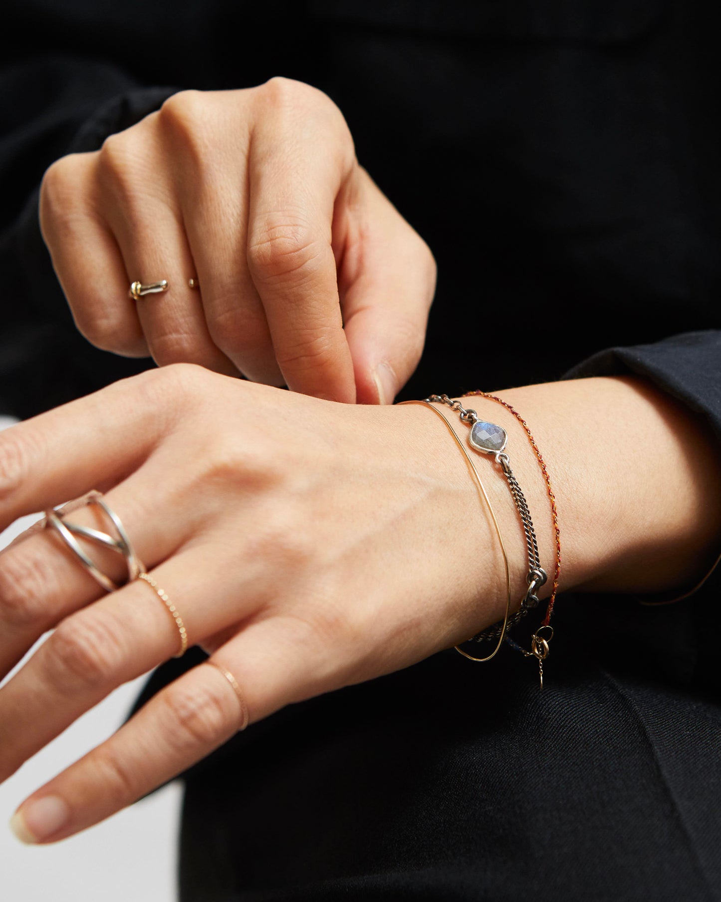 Close-up of hands wearing gold rings and bracelets on a dark background