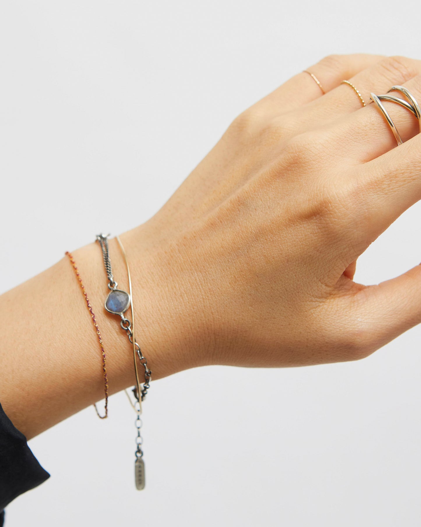 Hand wearing multiple bracelets and rings on a plain background
