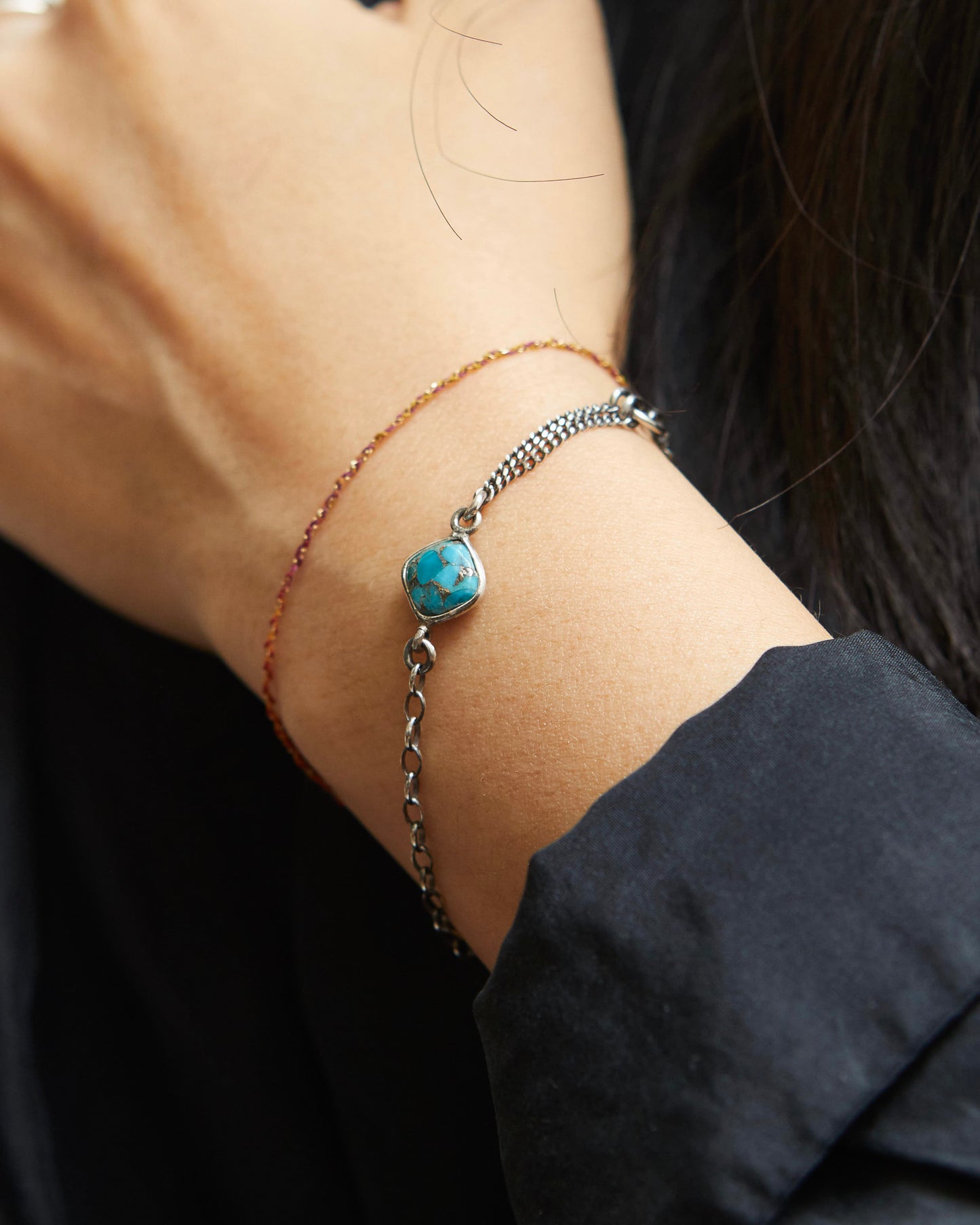 Close-up of a wrist wearing an antique silver bracelet with a turquoise stone against a dark background