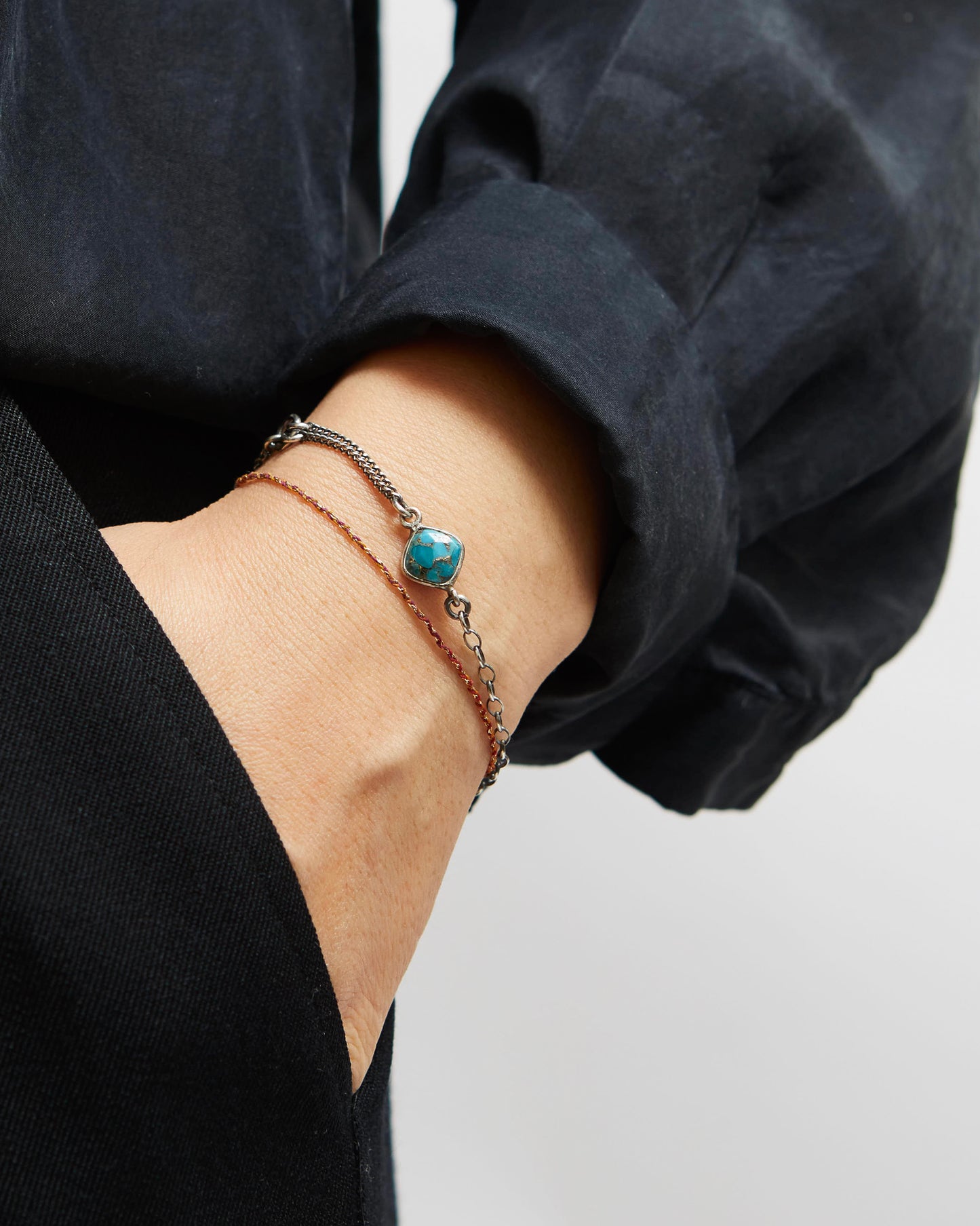 Close-up of a wrist wearing a bracelet with a blue stone, against a neutral background.