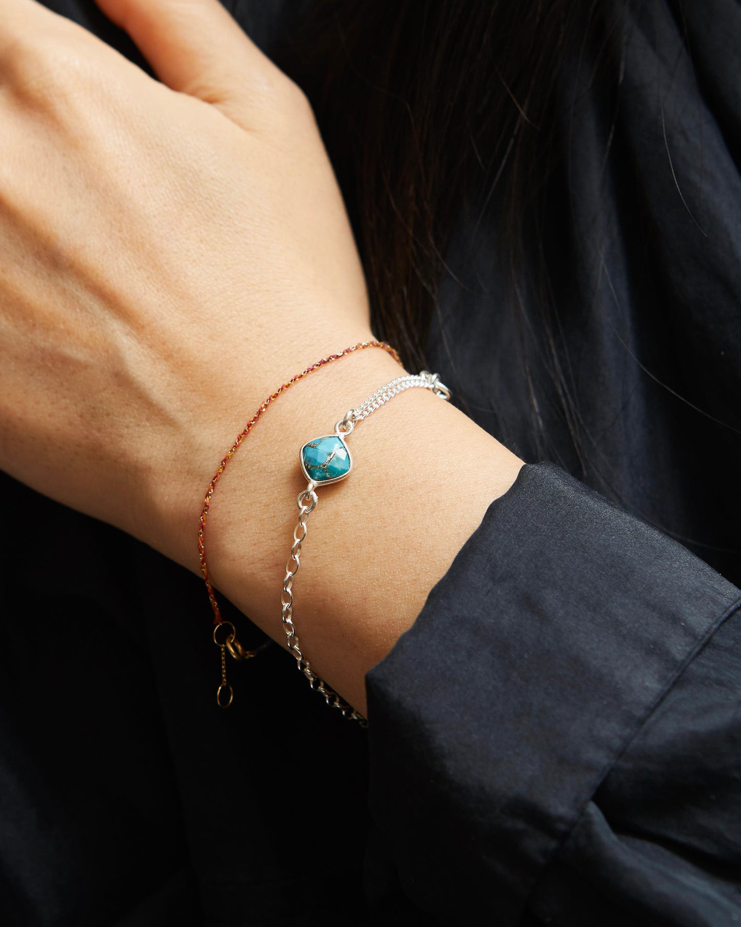 Close-up of a wrist wearing two bracelets with a dark background