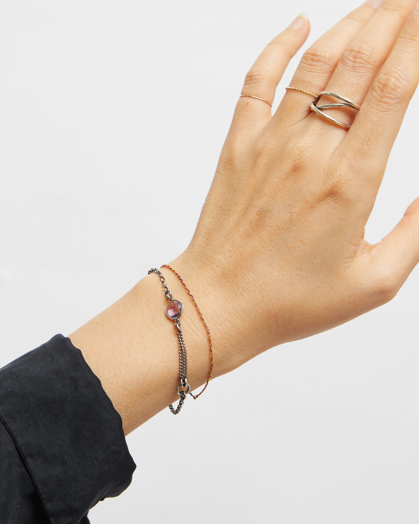 Hand wearing a ring and bracelet on a plain background