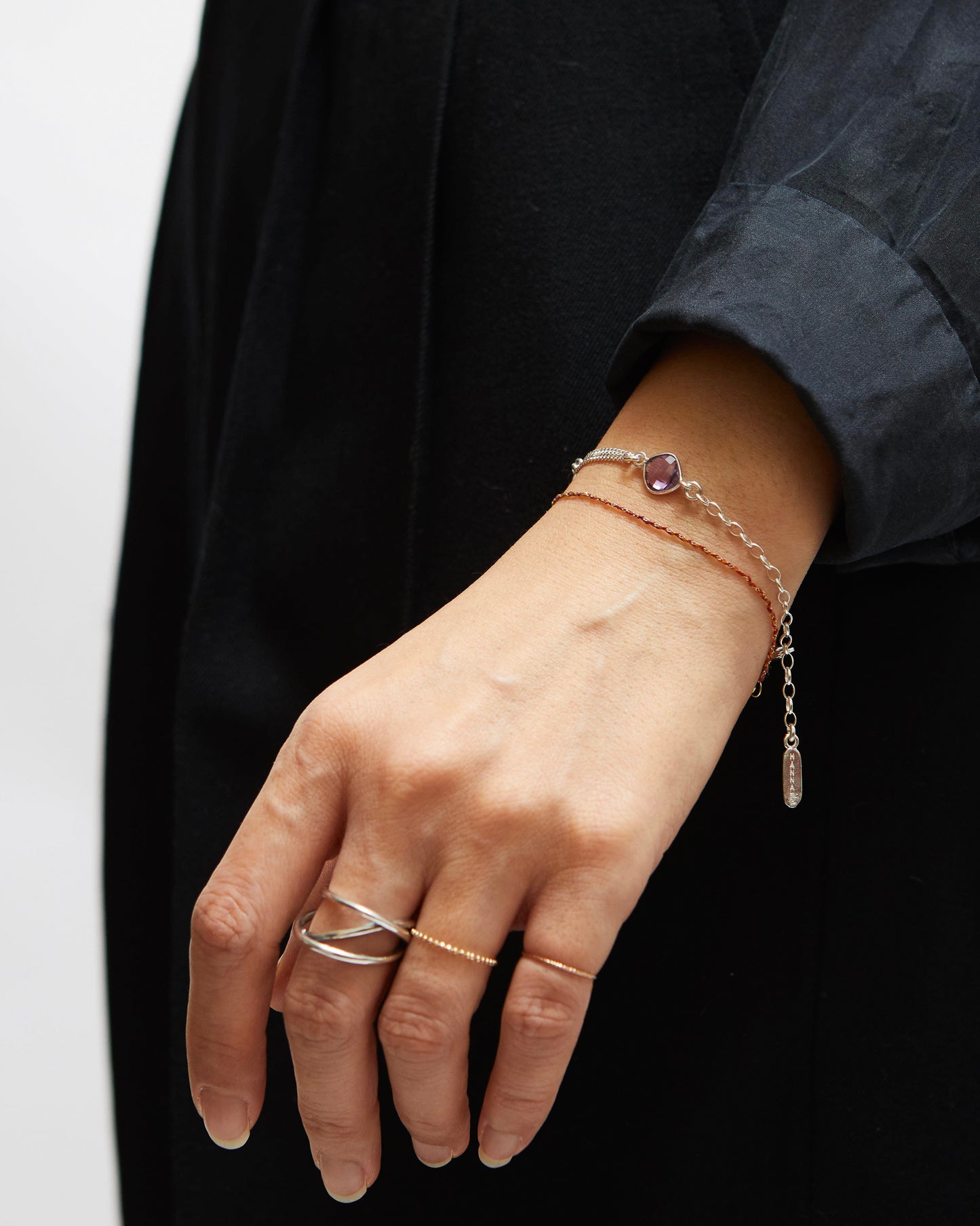 Hand wearing multiple bracelets and rings on a black background