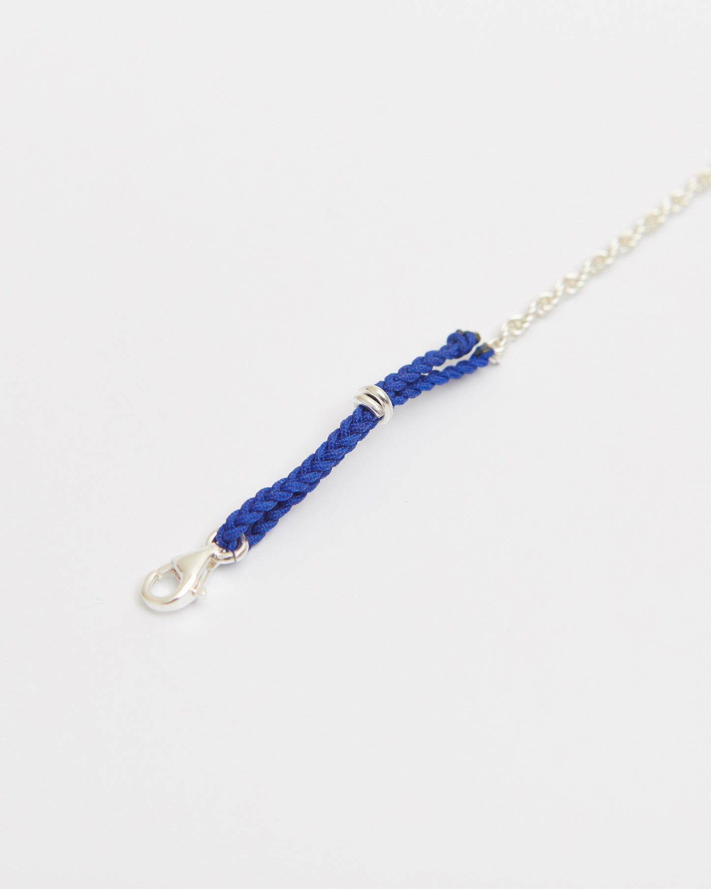 Close-up of sterling silver bracelet with braided cobalt blue cord detail and delicate silver chain on white background.