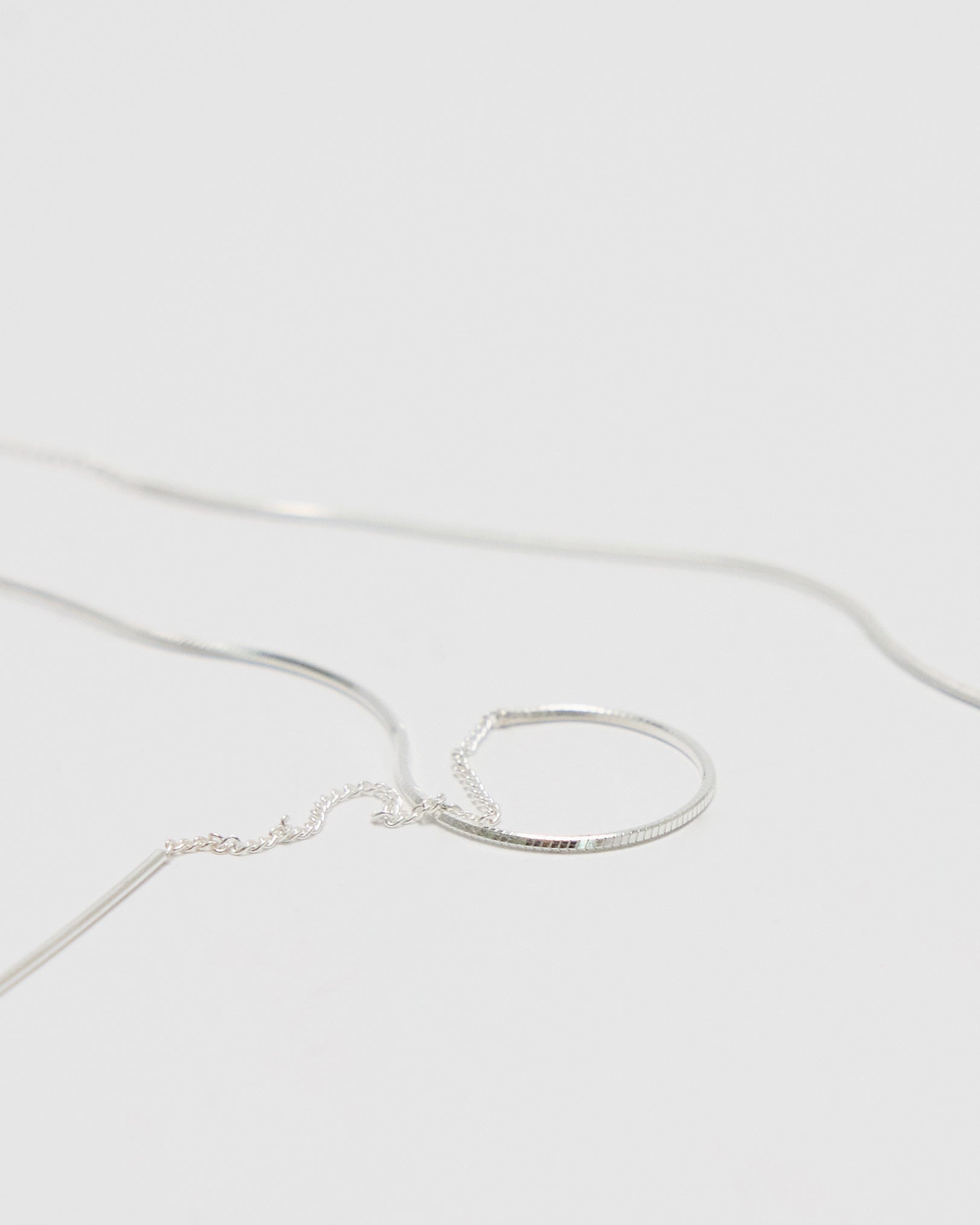 A delicate silver snake chain earrings with a minimalist, textured half-circle hoop pendant, photographed on a clean, light gray background.