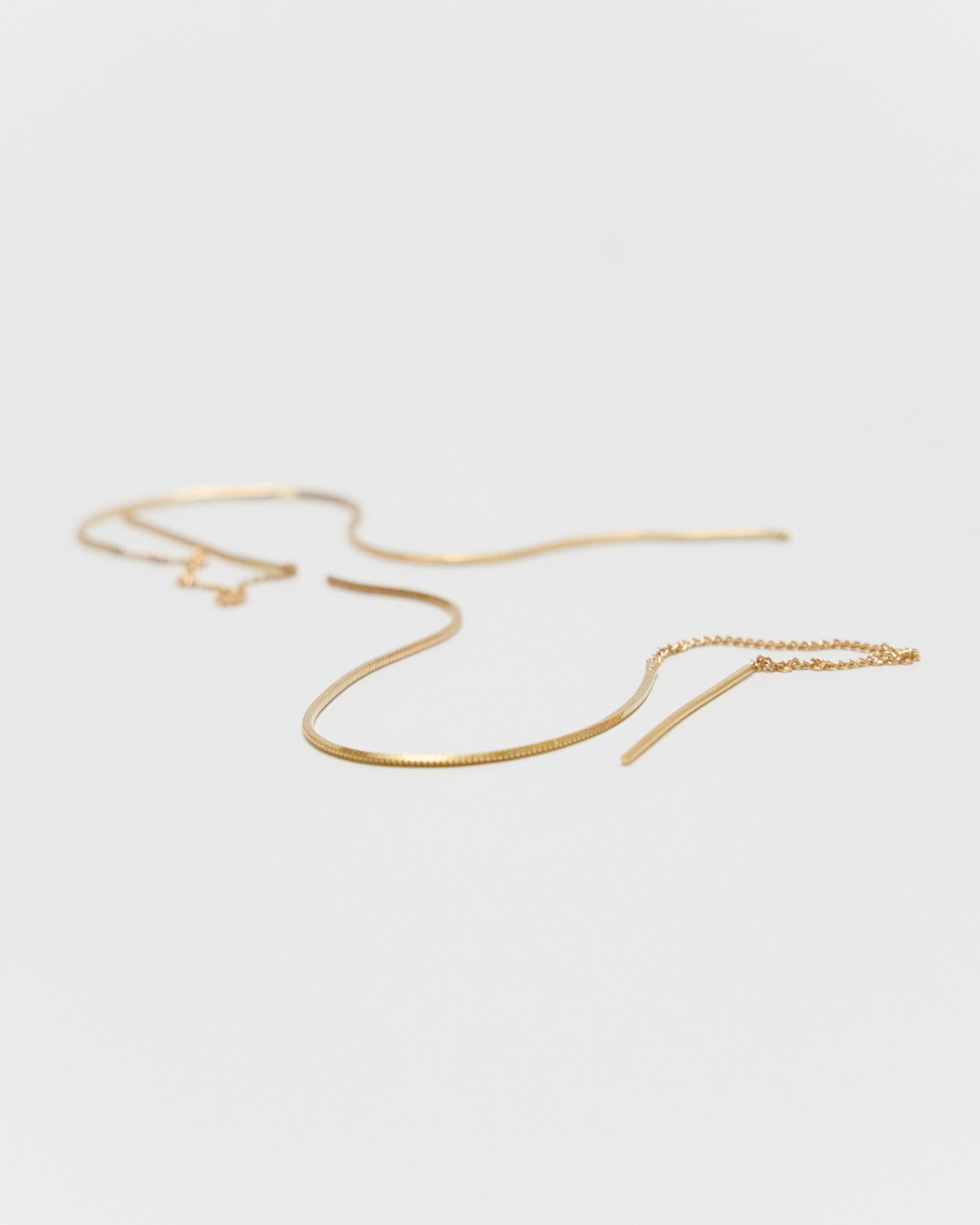 A delicate gold snake chain earrings with a matching small charm, displayed on a clean, light gray background.