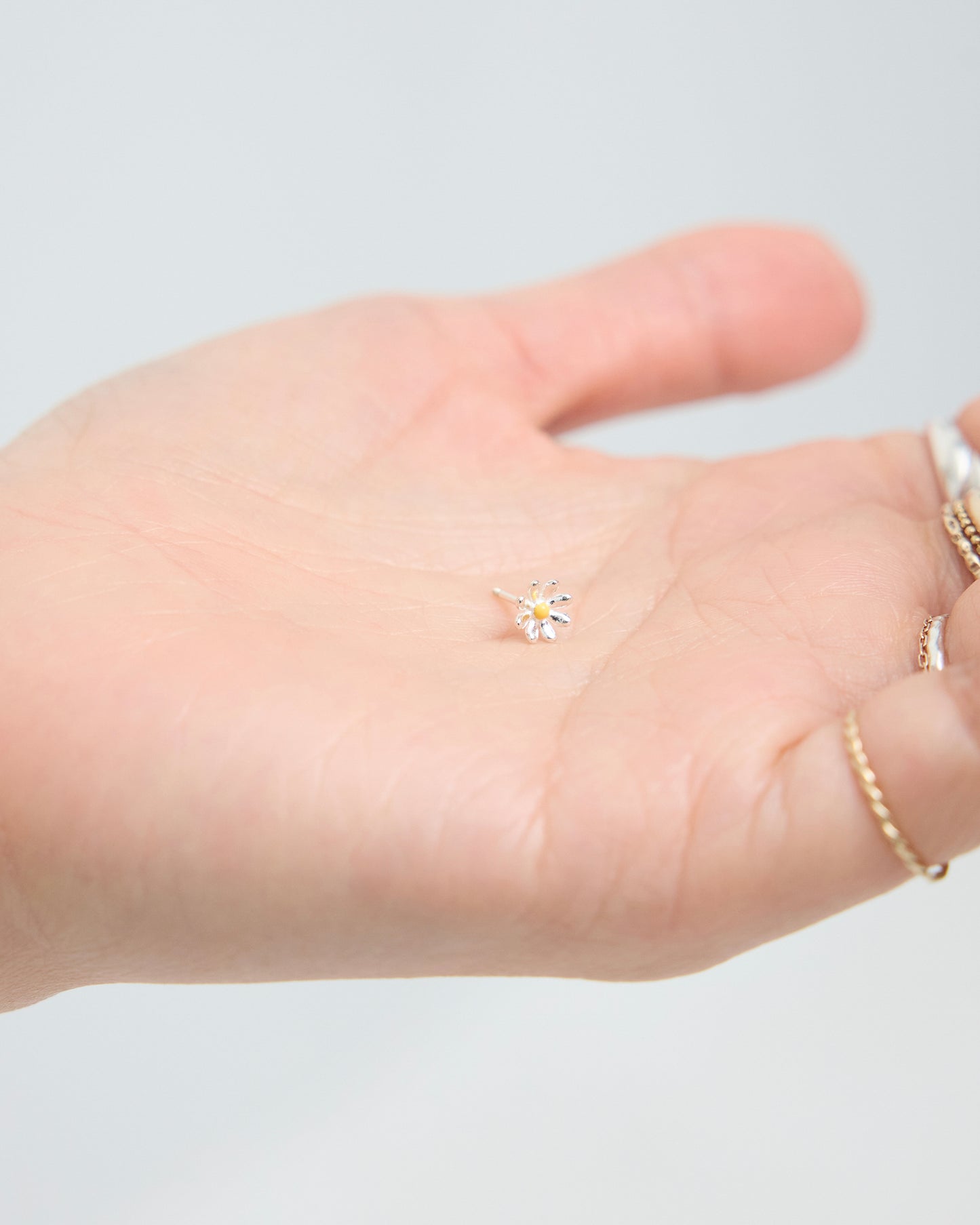 A tiny daisy stud earring resting on an open palm, showing its miniature scale, with silver petals and a soft yellow center.