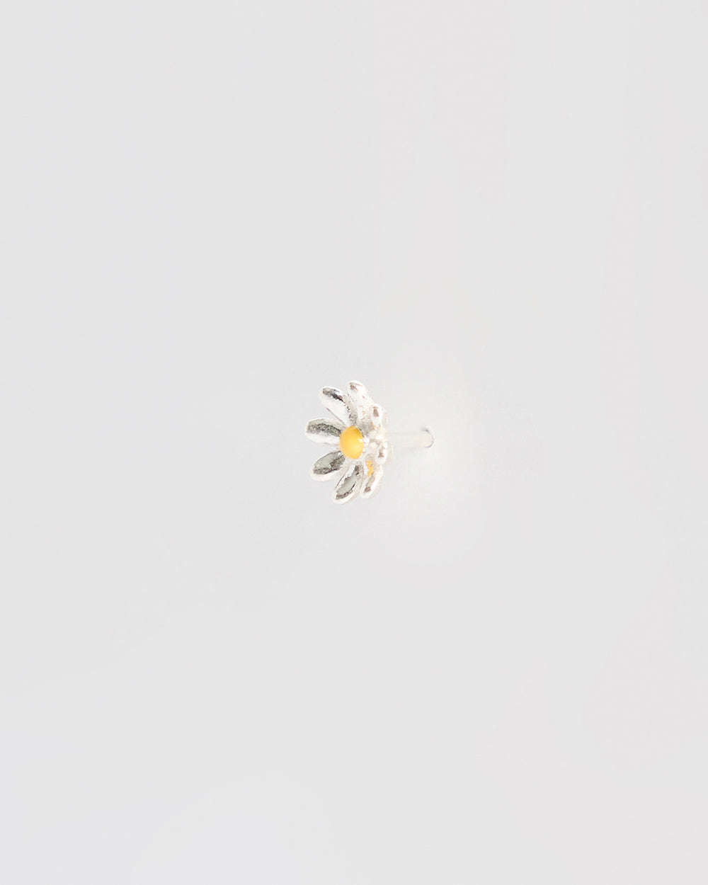 Side angle of a silver daisy stud earring showing the earring post and backing, with raised petal texture and a yellow enamel center.
